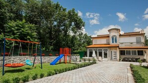 A playground with swings and slides, a paved walkway, and a building with a balcony. - Countryside Villa Tajo - Four Bedroom Holiday Home  with Swimming Pool (Imotski)