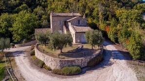 Une maison en pierre, avec un toit de tuiles, entourée d’un mur de pierre et bordée d’un chemin de gravier.