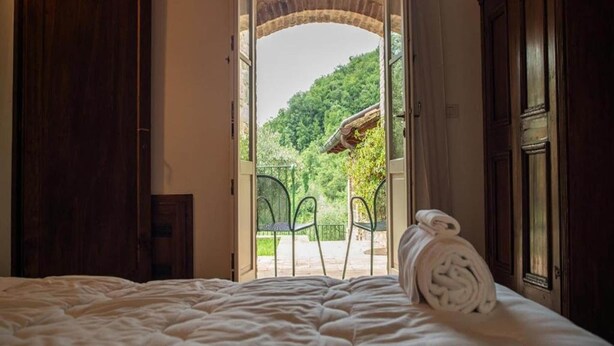 Une chambre à coucher avec un lit, une serviette enroulée, et une vue sur un jardin par une porte ouverte.