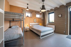 Quarto com beliches, uma cama de solteiro, uma mesa de cabeceira com luminária e janela com cortinas.