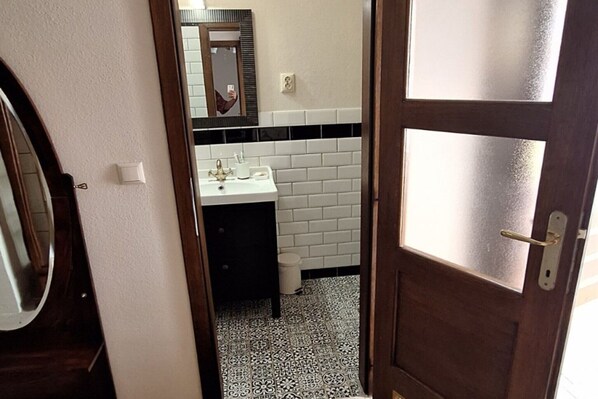 Uma casa de banho com uma pia branca, azulejos em tons de preto e branco, um espelho e uma porta com painéis de vidro jateado.
