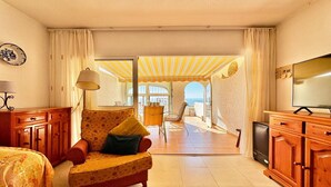 A cozy room with a sofa, a TV, and a view of the sea through an open door.