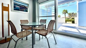 A modern room with a glass table and wicker chairs, a framed abstract painting, and a large window with a view of palm trees. - Apartment in Poblado Golf near Playa Serena (Roquetas de Mar)