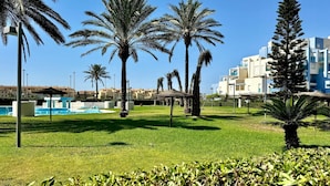 Zona de piscina con palmeras y un edificio al fondo.