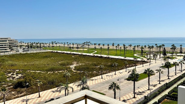 Un paseo marítimo con palmeras, pavimento a cuadros y vista al mar.