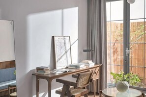 A room with a desk, books, a framed picture, a chair, a small table, and a potted plant. - Express by M Village Tu Xuong, a brand of Modern Village Lifestyle (Ho Chi Minh City)