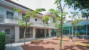 A modern building with a courtyard, featuring a mix of trees and benches, and a glass facade on one side. - Express by M Village Tu Xuong, a brand of Modern Village Lifestyle (Ho Chi Minh City)