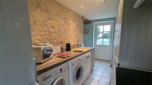 Een kleine keuken met een stenen muur, een wasmachine, een magnetron en een spoelbak.
