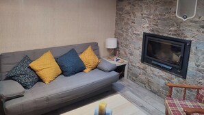 Ein Wohnzimmer mit grauem Sofa, Steinwand, Kamin und Oberlichter.