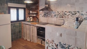 Eine kleine Küche mit Einbauofen, Spüle und Kaffeemaschine. Zwei Pendelleuchten, ein Fenster mit Vorhängen und ein Regal mit Gläsern.