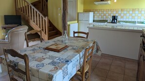 A dining area with a table set for two, a wooden chair, a white sofa, and a staircase leading to another room. - Peaceful lodging near Orleans, pets allowed, terrace and garden (Vennecy)