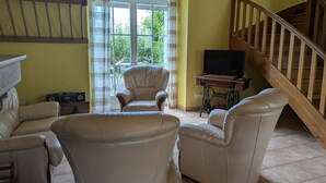 A living room with a sofa, armchairs, a television on a wooden table, and a staircase. - Peaceful lodging near Orleans, pets allowed, terrace and garden (Vennecy)