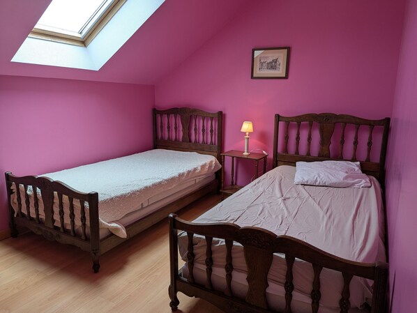 Une chambre avec deux lits en bois, un puits de lumière et un tableau encadré au mur.