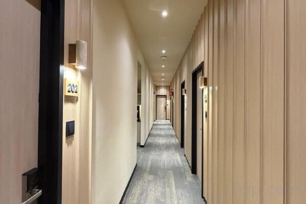 Pasillo de hotel con puertas a ambos lados, placas de habitaciones numeradas y suelo alfombrado.
