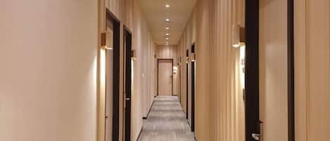 Un couloir d’hôtel avec des portes de chaque côté, un éclairage encastré et un sol recouvert de moquette.