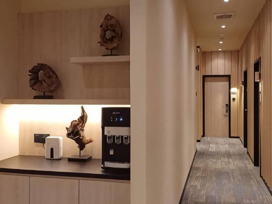 A hallway with a coffee machine, a lighted wall, and a door at the end.