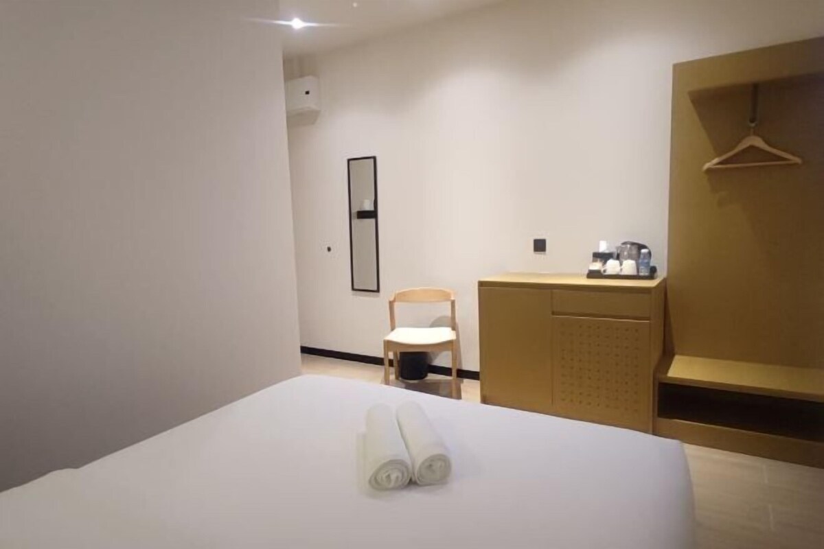 A hotel room with a bed, a chair, a desk with a coffee machine, and a coat hanger.