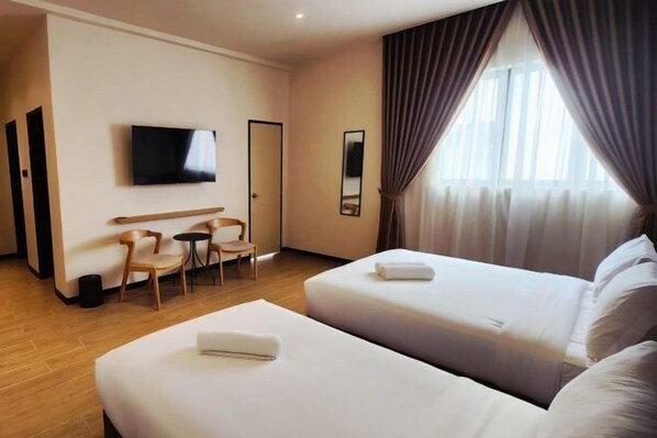 Une chambre d’hôtel avec deux lits, une télévision, un bureau avec des chaises et une fenêtre avec des rideaux.
