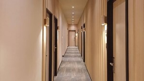Un largo y estrecho pasillo de hotel con puertas a ambos lados, iluminación empotrada y suelo alfombrado.