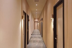Ein langer, schmaler Hotelkorridor mit Türen an beiden Seiten, eingelassener Beleuchtung und Teppichboden.