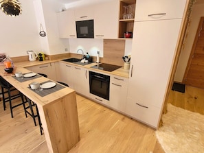Une cuisine moderne avec des meubles de couleur bois clair, un îlot central, un four encastré et un four à micro-ondes.