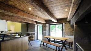 Un intérieur rustique avec un mur en pierre, des poutres en bois au plafond, un sol en pierre, une table en bois et un banc.