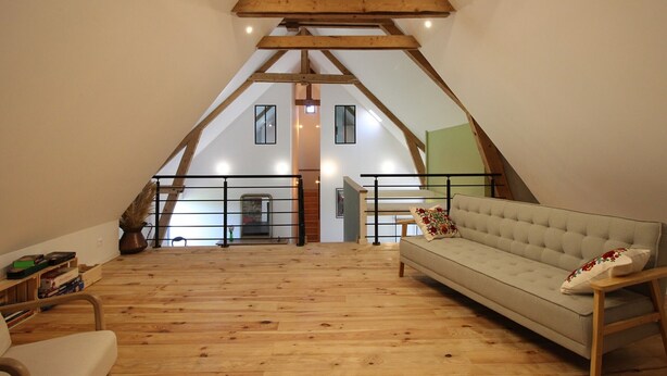 Une chambre spacieuse aménagée en mezzanine, avec un plafond haut, des poutres en bois, un canapé et une vue sur l’intérieur.