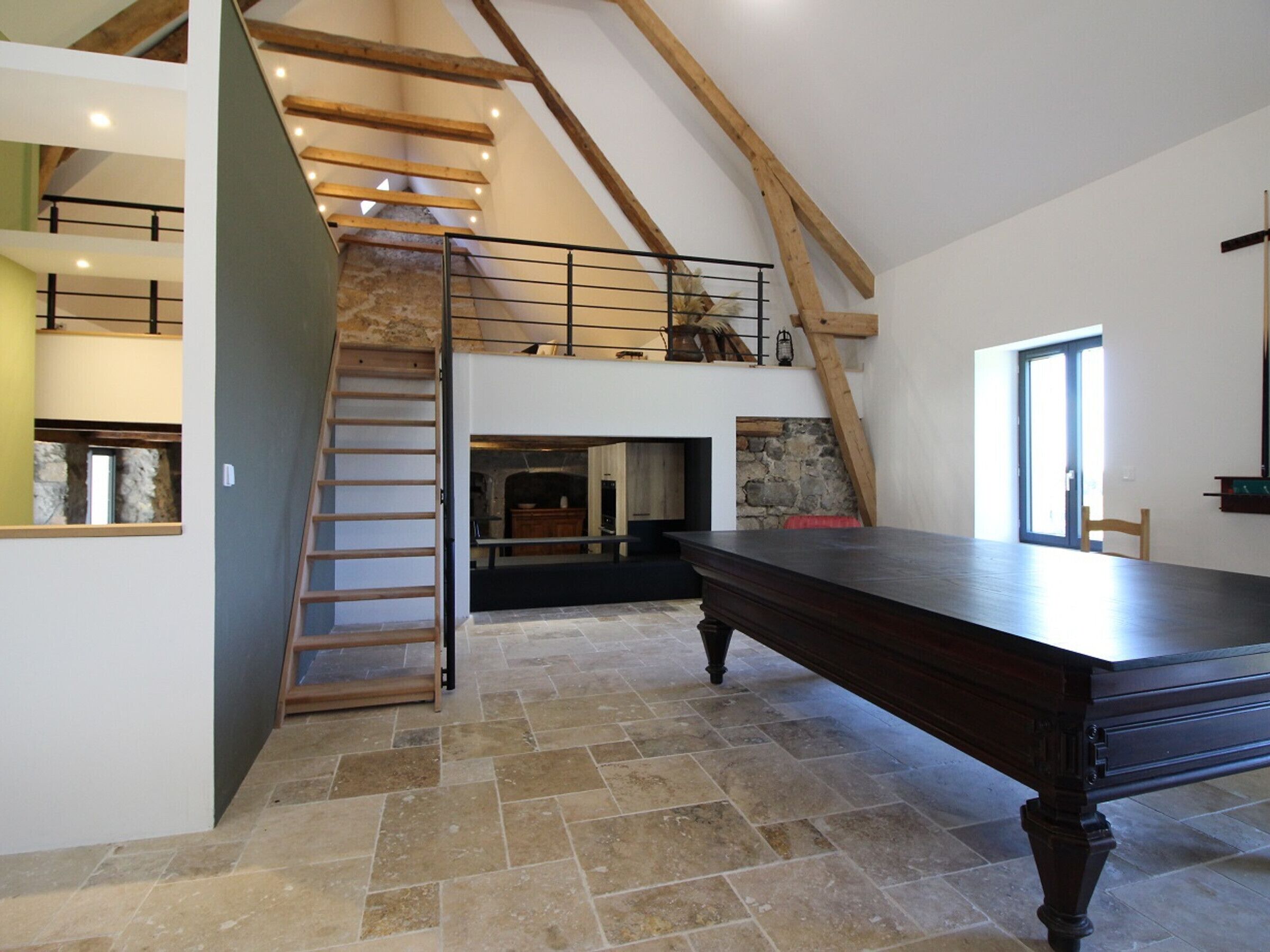Un loft amplio con techo alto, vigas de madera a la vista, chimenea de piedra y una gran mesa de comedor.