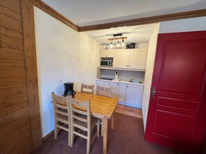A compact kitchen with wooden cabinets, a dining table with chairs, a red door, and a coffee maker.