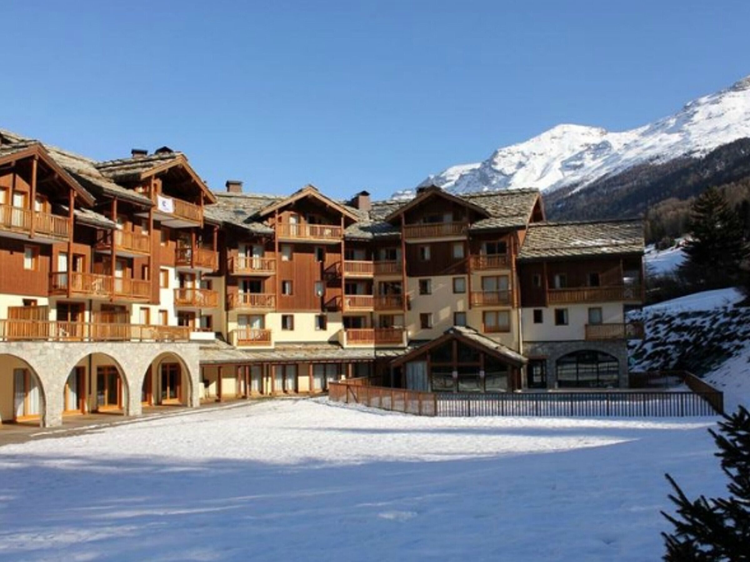 A multi-story wooden lodge with balconies, set against a snowy mountain backdrop.