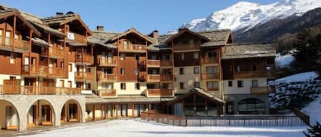 Una cabaña de madera de varios pisos con balcones, frente a un paisaje montañoso nevado.