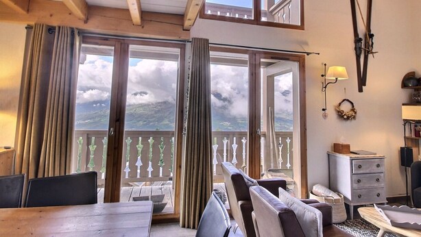 A room with a wooden ceiling, large sliding glass doors, a dining table, and a sofa.