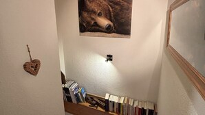 A room with a wooden bookshelf filled with books, a framed picture of a dog on the wall, and a heart-shaped decoration on the left.