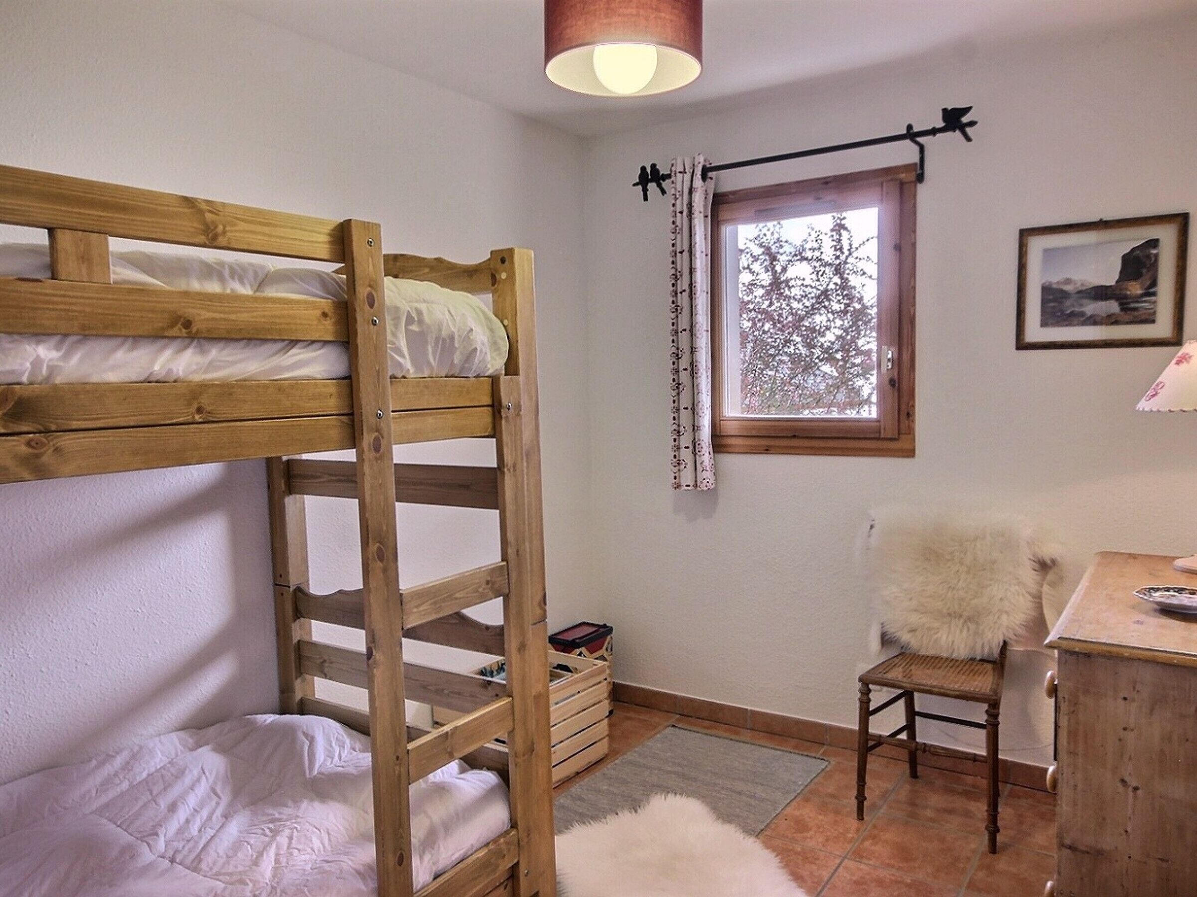 Habitación con literas, escritorio, silla, ventana con cortinas e imagen enmarcada en la pared.