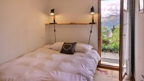 A bedroom with a bed, two bedside lamps, a window with a view of greenery, and a hanging light fixture.