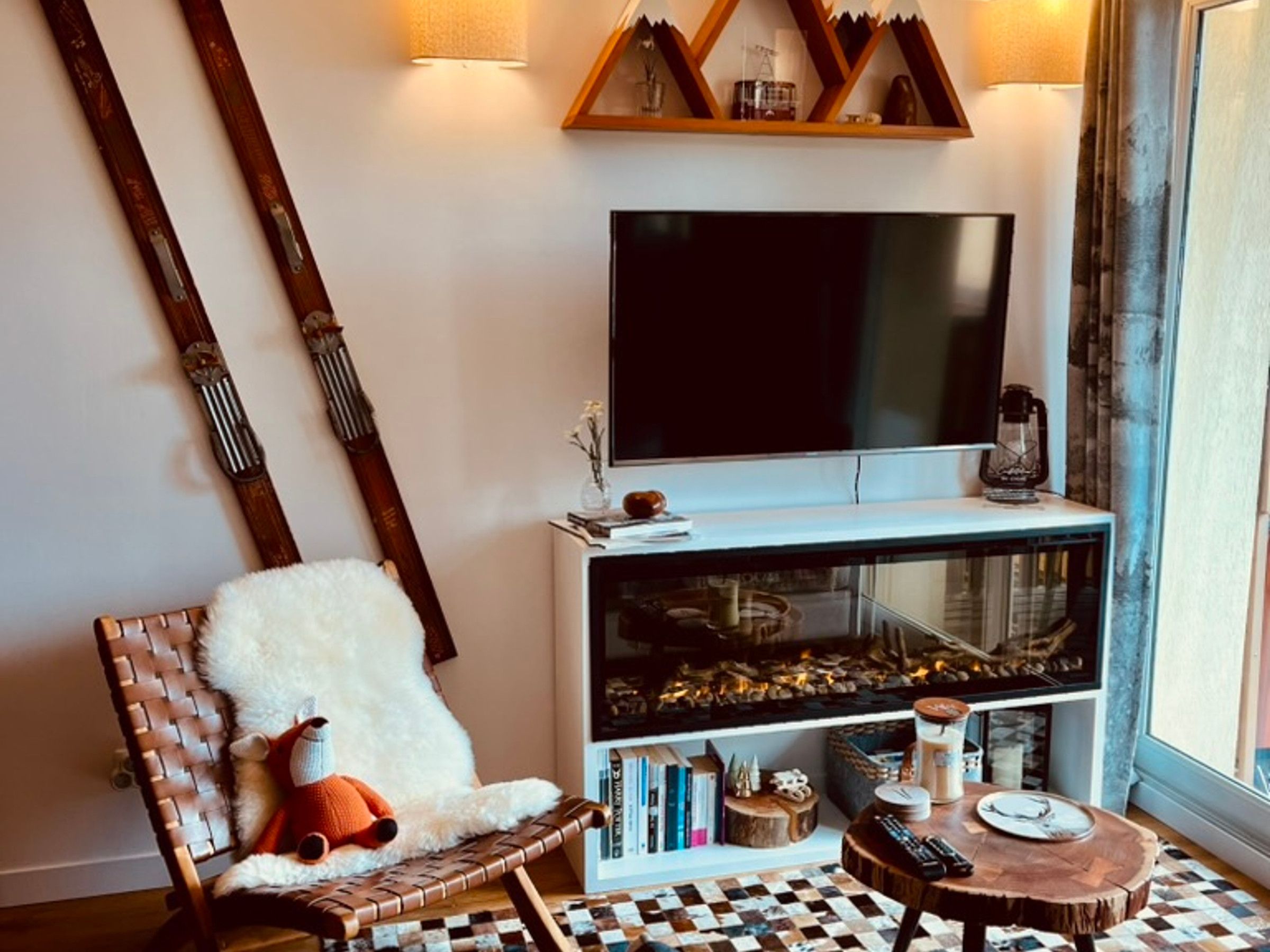 A cozy living room with a flat-screen TV, a fireplace, a woven chair, and a small round table.