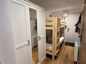 A room with a bunk bed, white wardrobe, and a coat hanging on the wall.