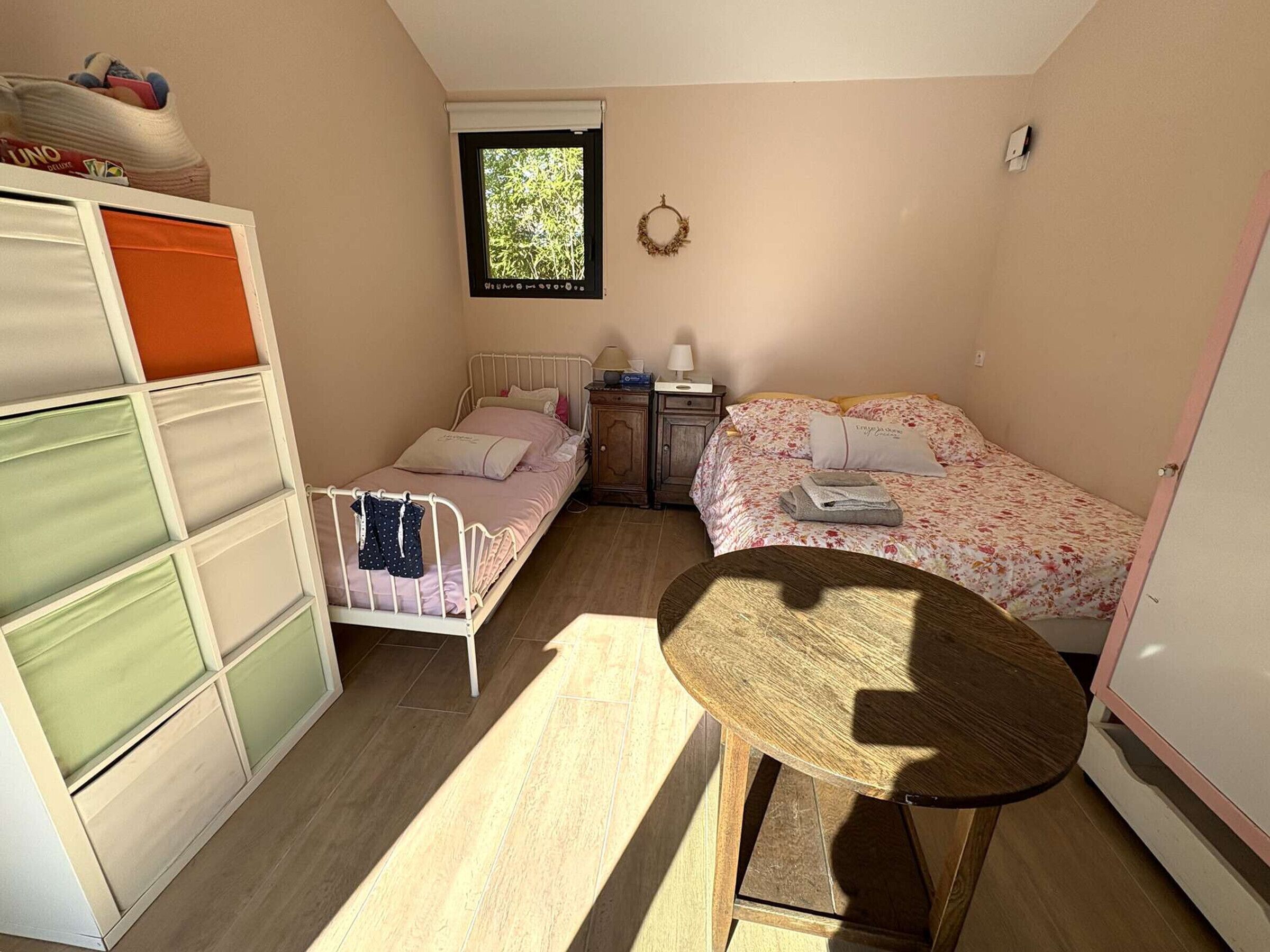 Un dormitorio pequeño y acogedor con dos camas individuales, una mesa de madera y un ventanal que proporciona luz natural.