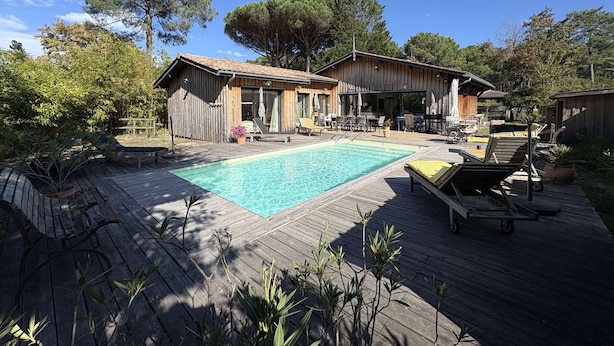 Eine Holzterrasse mit Swimmingpool, Liegestühlen und einem überdachten Sitzbereich im Freien.