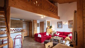 Un intérieur chaleureux avec une table à manger en bois, des canapés rouges et un coin cuisine doté de meubles en bois.