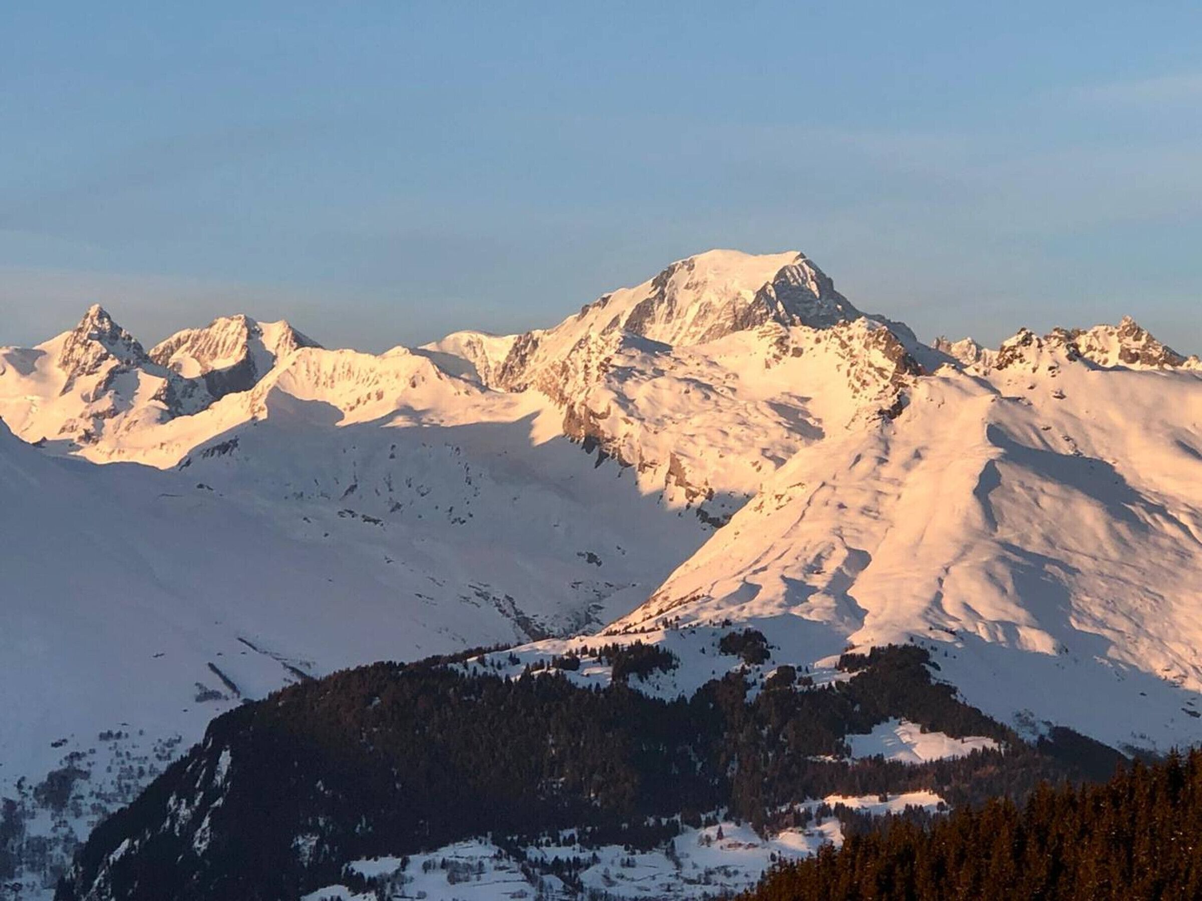 Un paysage montagneux avec des sommets enneigés et une vallée boisée.