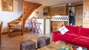 Un salon chaleureux avec un canapé rouge, une table basse en bois et un escalier menant à la cuisine.