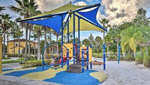 Un parque infantil con una estructura para escalar, un tobogán y una zona sombreada con toldo.