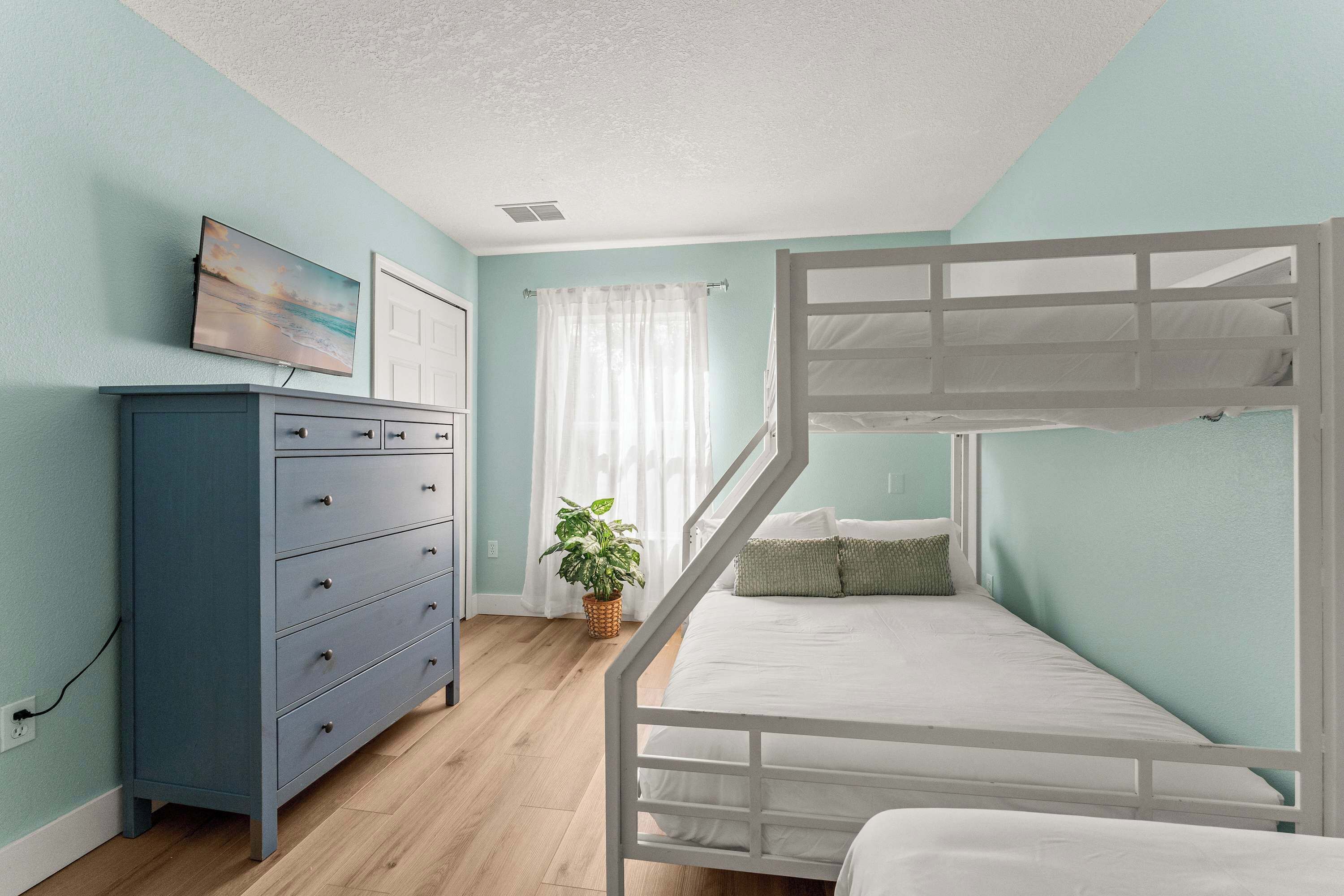 A bedroom with a bunk bed, a dresser, a plant, and a painting on the wall.
