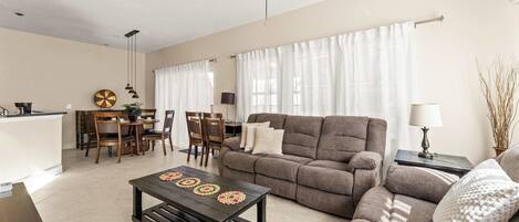 A living room with a sofa, a coffee table, a dining area with chairs and a table, and a kitchen area.