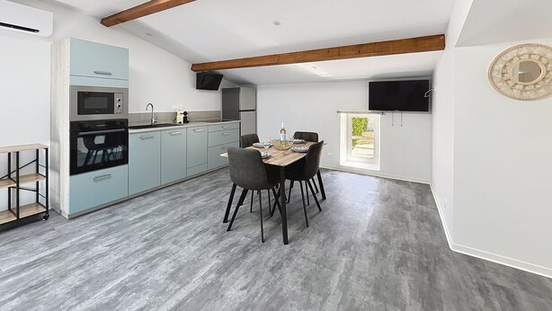 Una cocina moderna con tragaluz, un comedor con mesa y sillas, y un televisor montado en la pared.