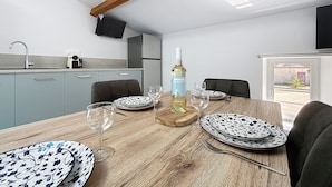 Una mesa de comedor con platos, una botella y vasos, ubicada en una habitación con cocina y televisor.