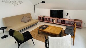 Een moderne woonkamer met een bank, twee stoelen, een salontafel, een televisie en een boekenkast.