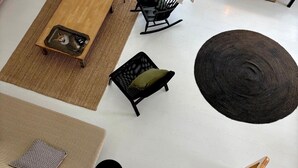 Een ruime woonkamer met een houten salontafel, een zwarte schommelstoel, een zwarte bank, een rond vloerkleed en een trap.