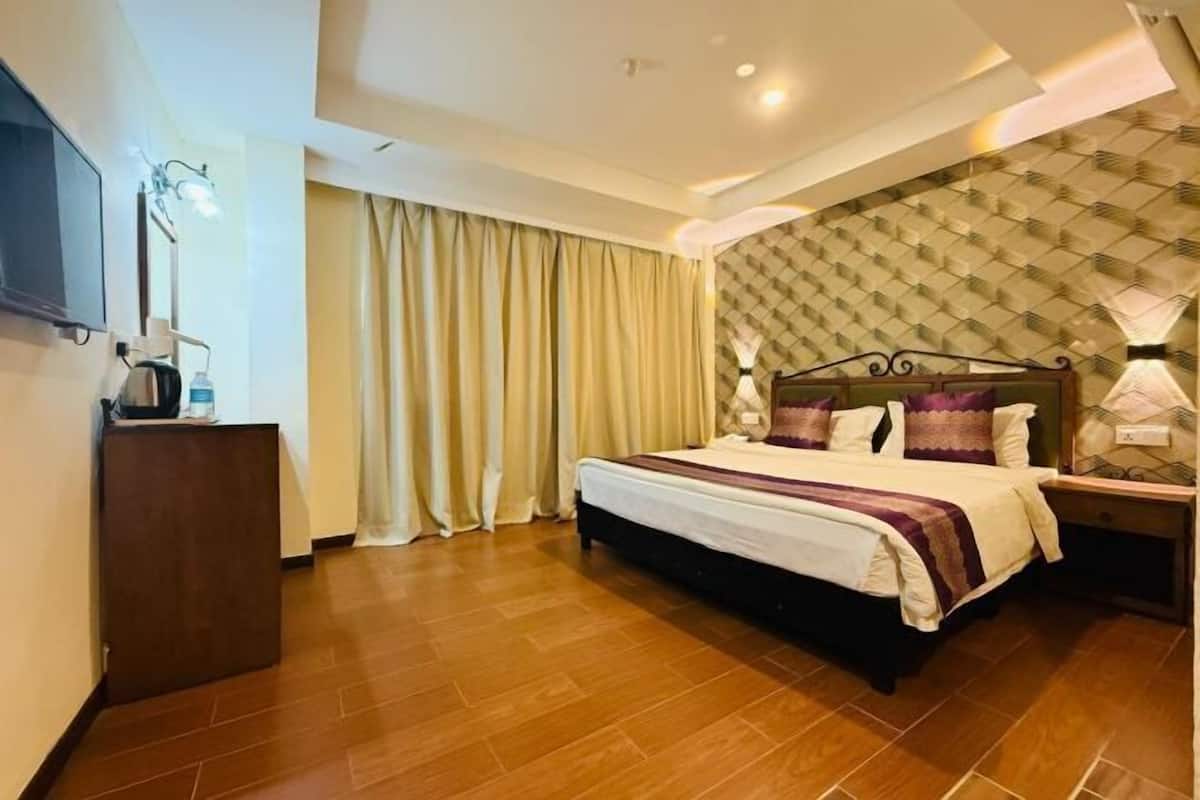 A hotel room with a bed, curtains, a desk with a lamp, and a television.